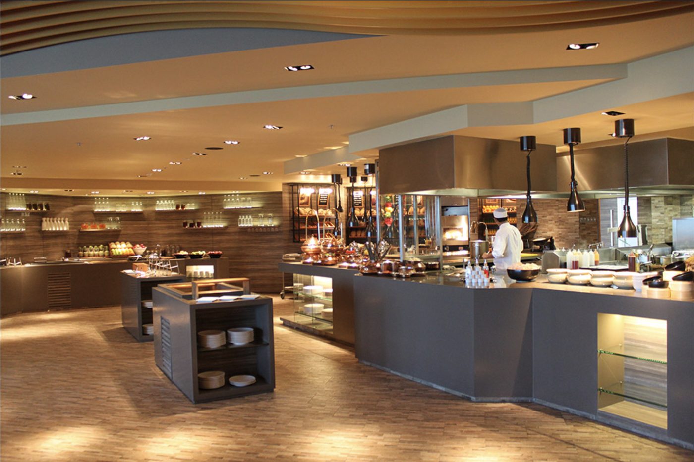 Open live-cooking stations in a hotel restaurant under stainless steel canopies